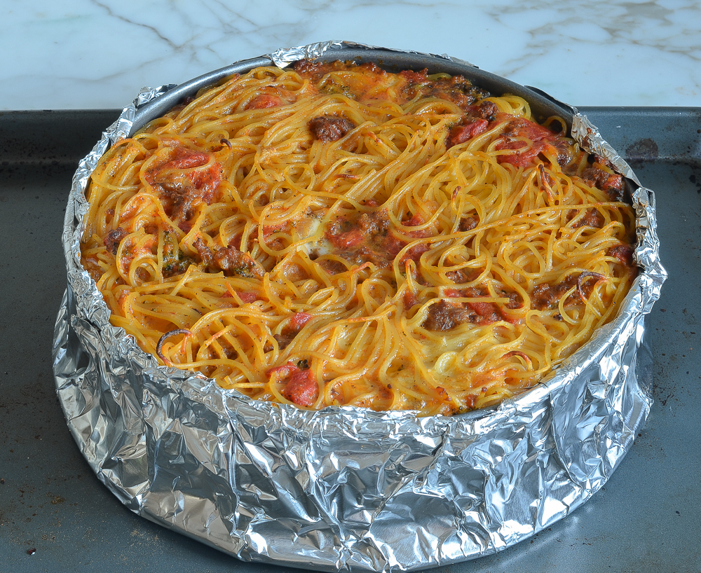 Spaghetti pie in a pan wrapped in foil.