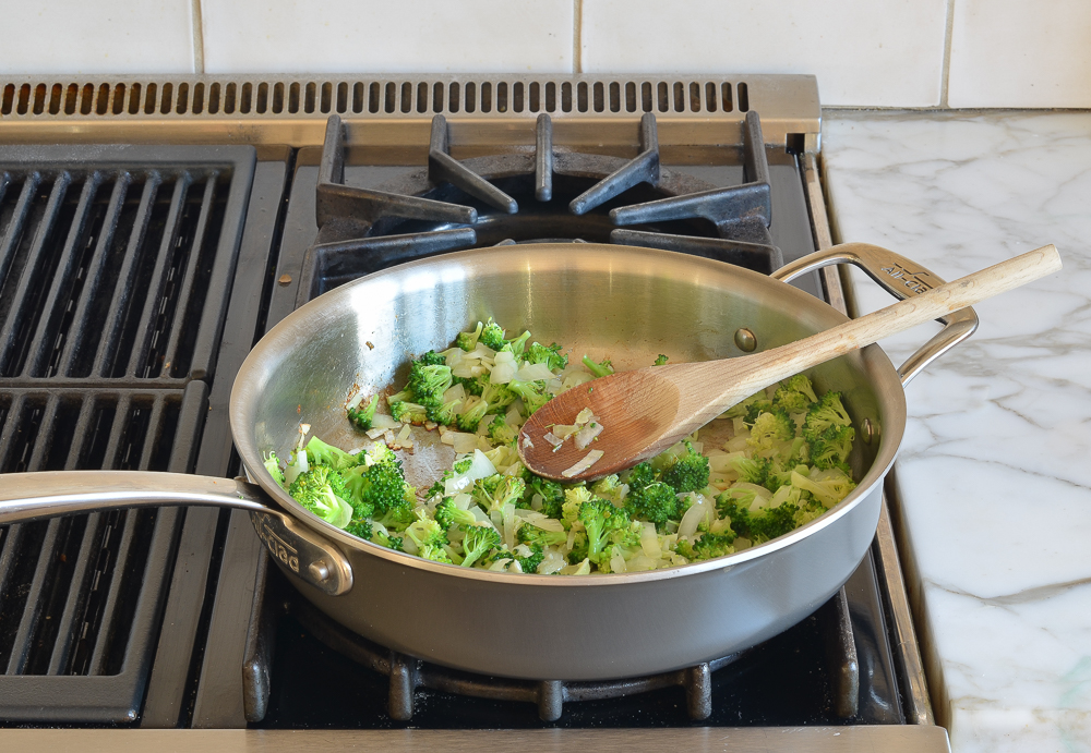 Broccoli in a skillet with onion and garlic.