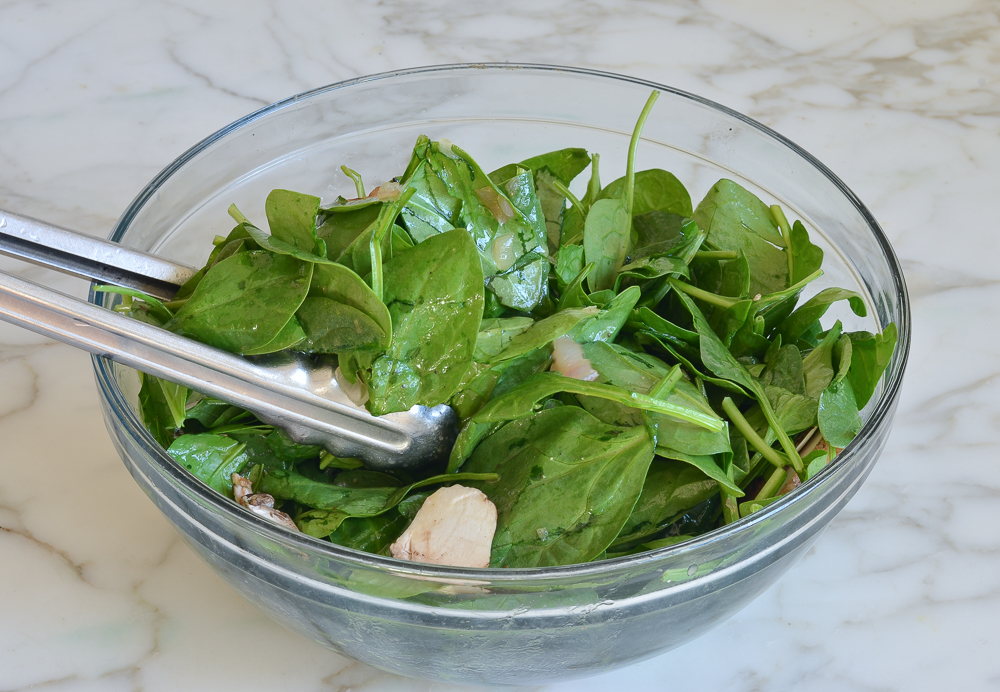 Spinach and mushrooms being tossed with a warm bacon dressing.