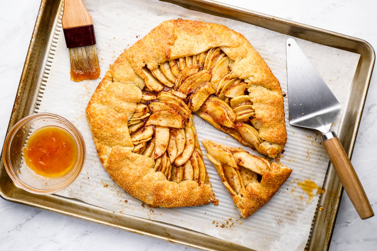 apple tart sliced on baking sheet with bowl of apricot jam for brushing