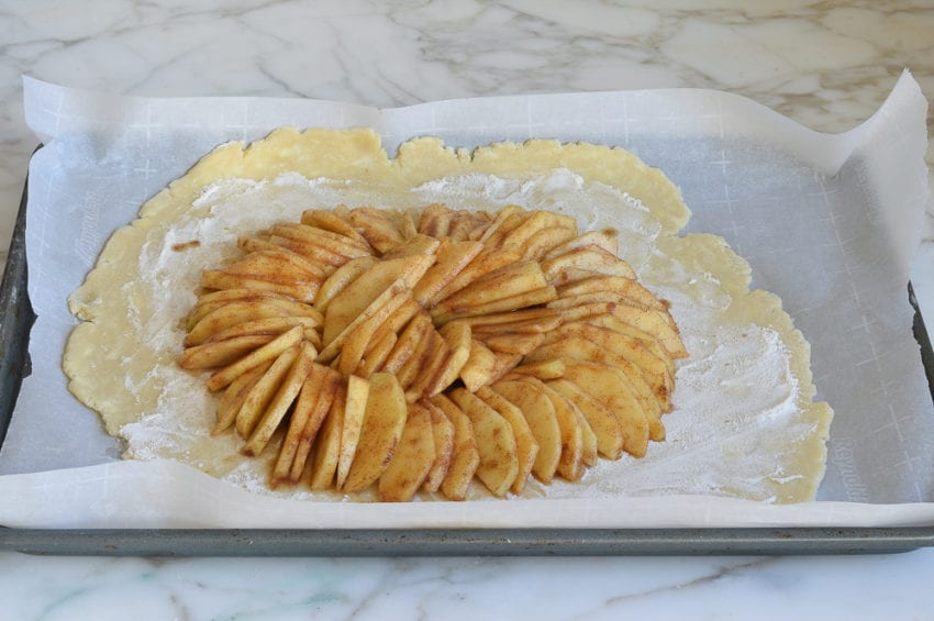 Seasoned apple slices arranged in the center of dough on a lined baking sheet.