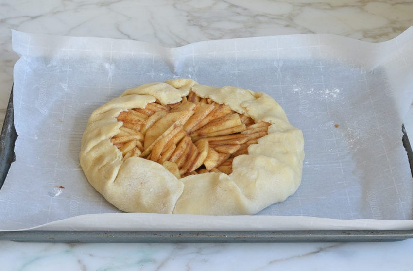Seasoned apples in folded dough on a lined baking sheet.