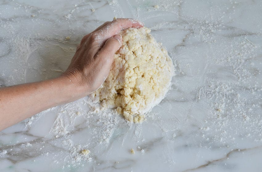Person pushing together crumbly dough.