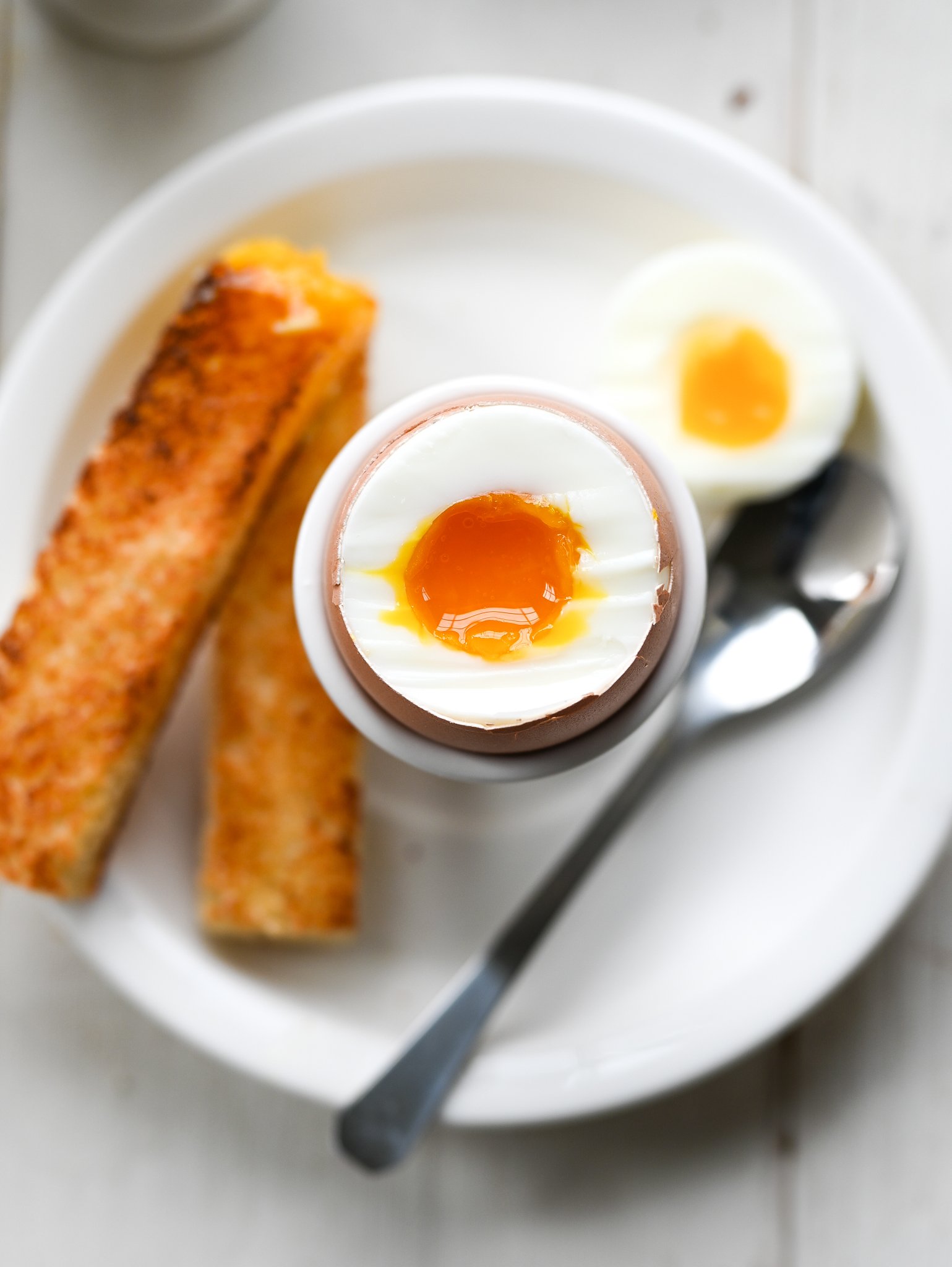 Soft-boiled egg in egg cup next to toast soldiers.