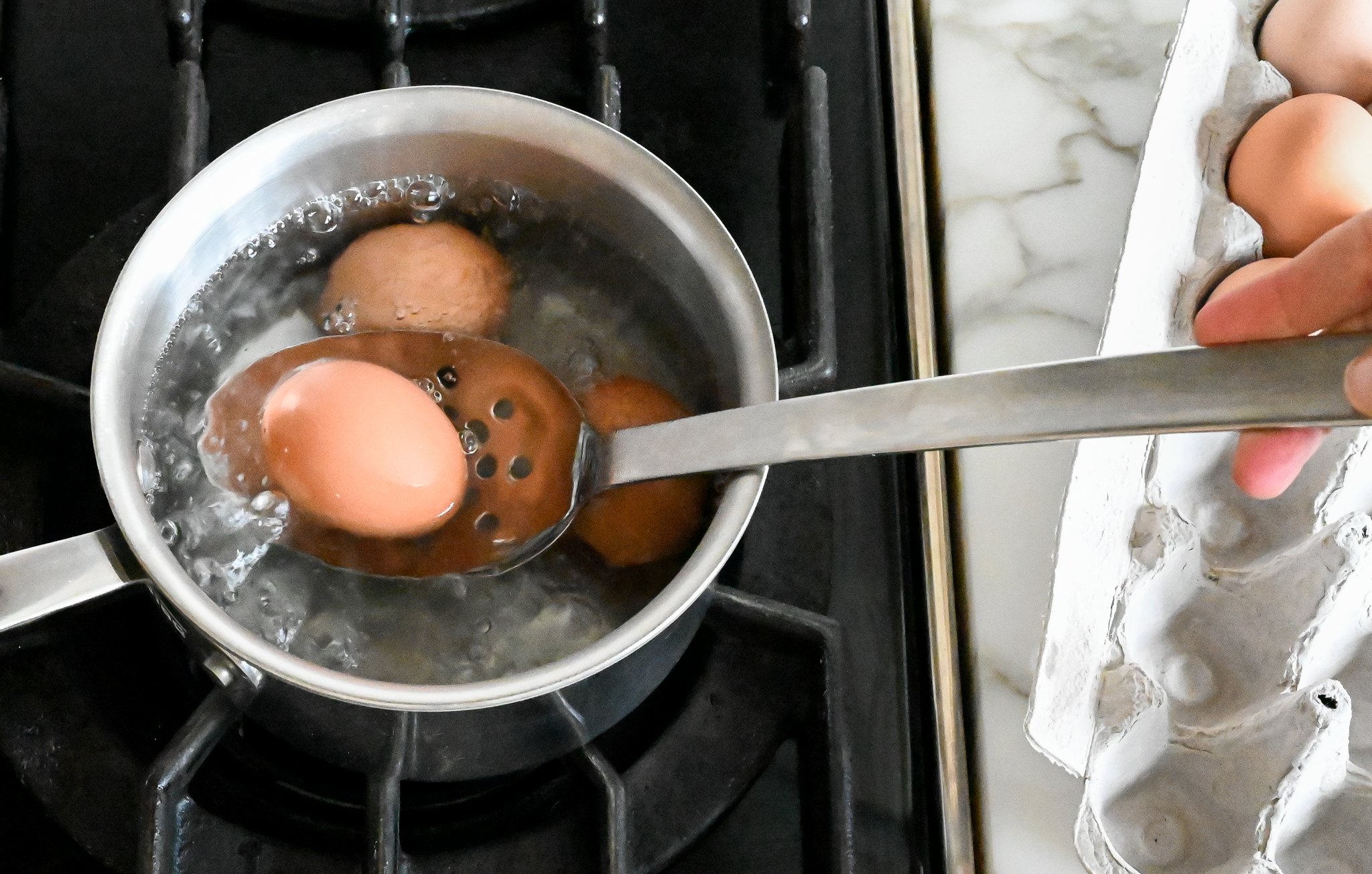 Lowering eggs into boiling water using a slotted spoon.