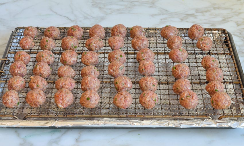 Uncooked meatballs on a wire rack over a lined baking sheet.