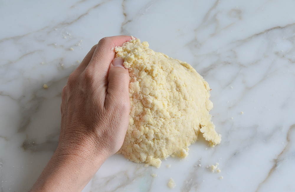 Person pushing crumbly dough into a mound.