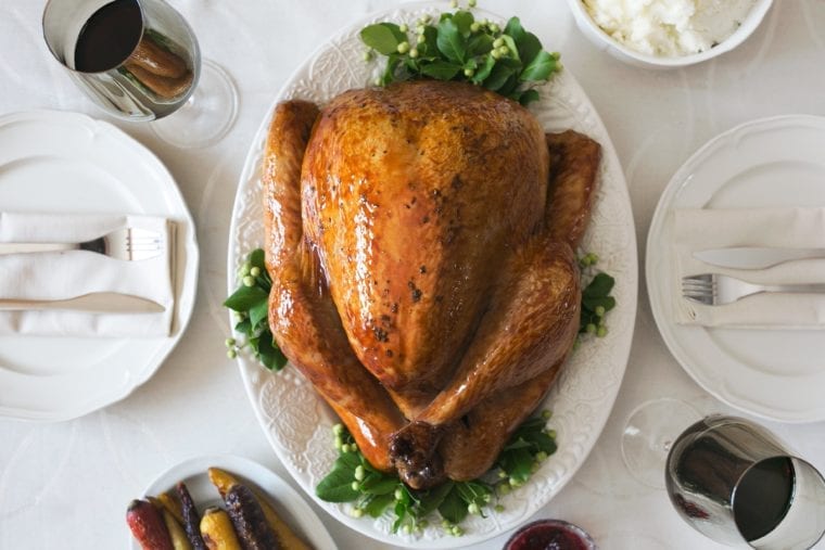 Holiday table set with roast turkey and glasses of red wine.