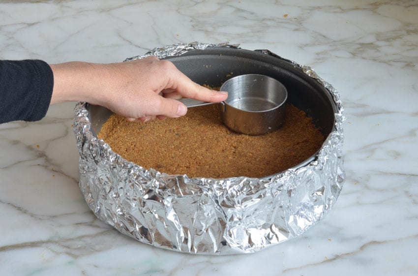 Person pressing graham cracker mixture into a pan with a measuring cup.