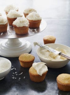 Coconut cupcakes on and around an elevated platter.