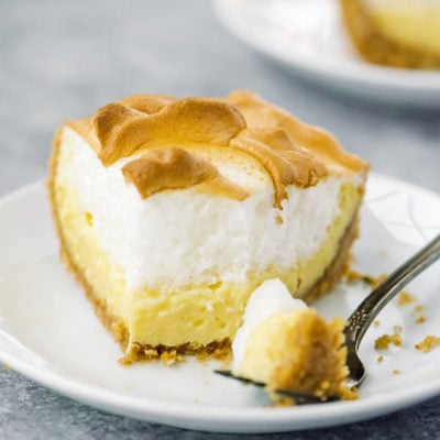 Slice of lemon meringue pie on a plate with a fork.