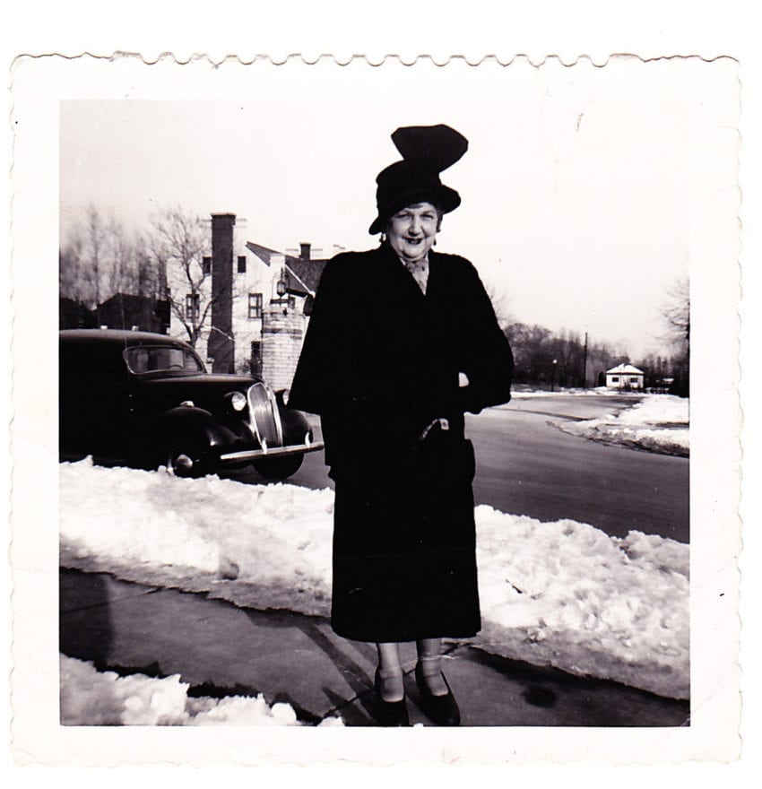Black and white picture of a woman standing on a sidewalk next to snow.