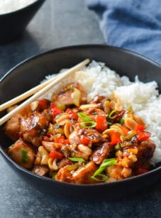 Chopsticks on a bowl of Kung Pao chicken with rice.