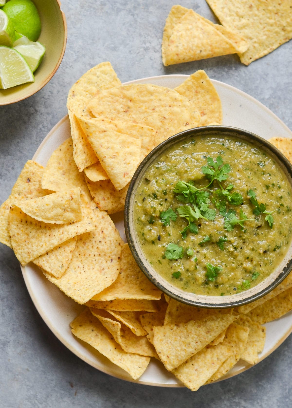 Bowl of salsa verde on a plate with tortilla chips.