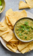 Bowl of salsa verde on a plate with tortilla chips.