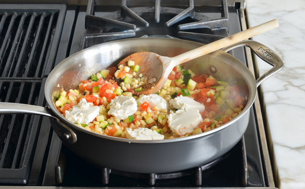 Chunks of goat cheese over vegetables in a skillet.