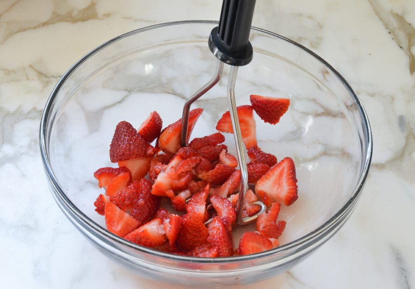 Potato masher in a bowl with strawberries.