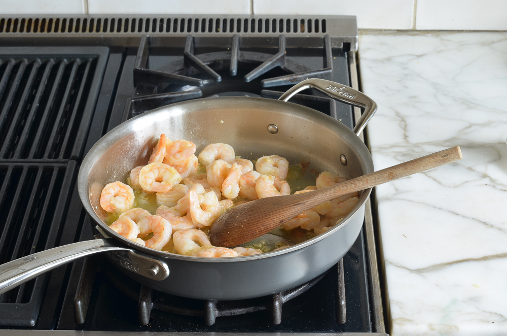 Wooden spoon stirring a pan of shrimp.