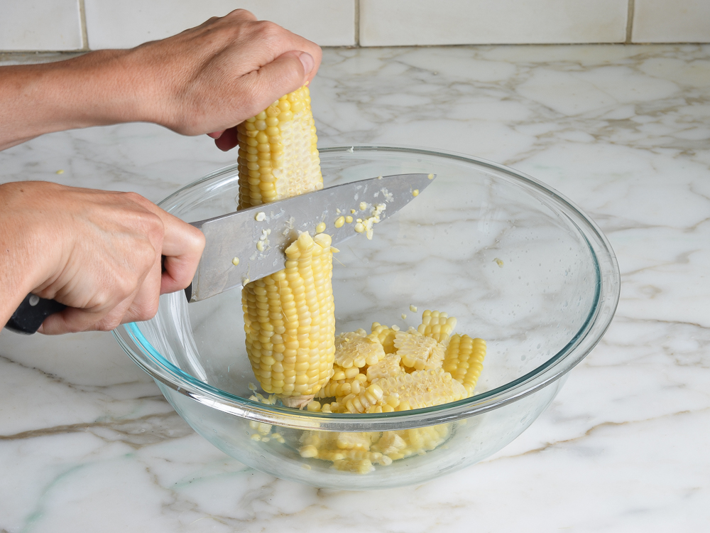 Person using a knife to shave corn off of a cob.