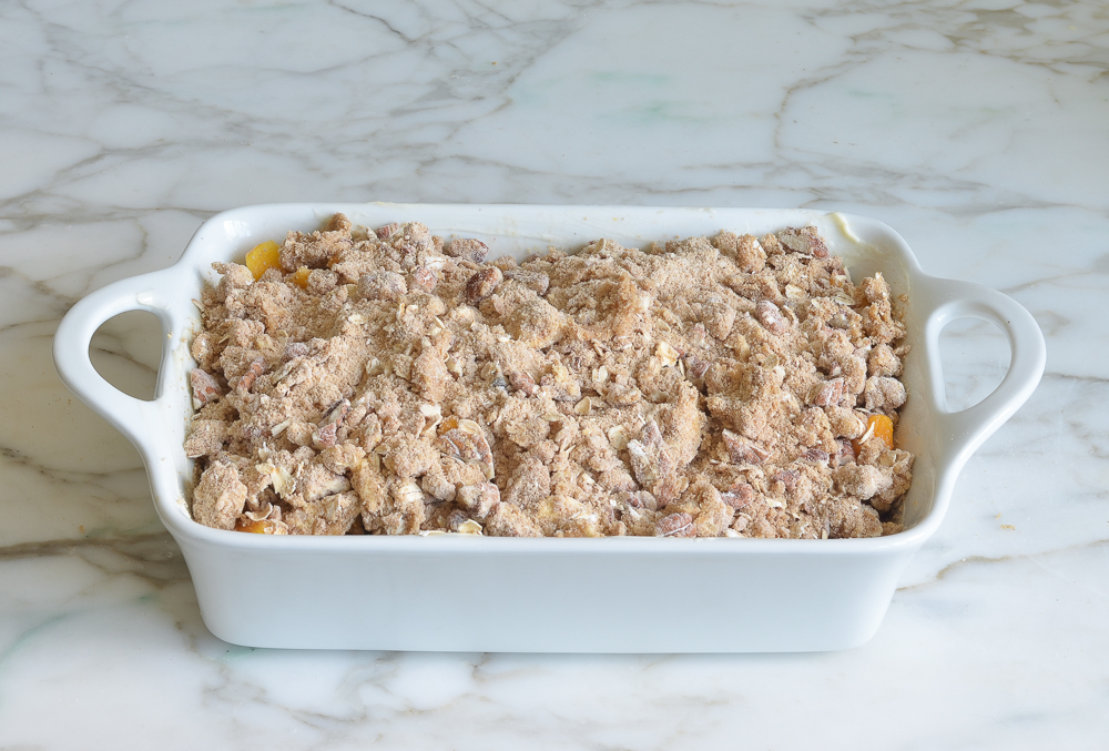 Baking dish of peaches topped with a nut and oat mixture.