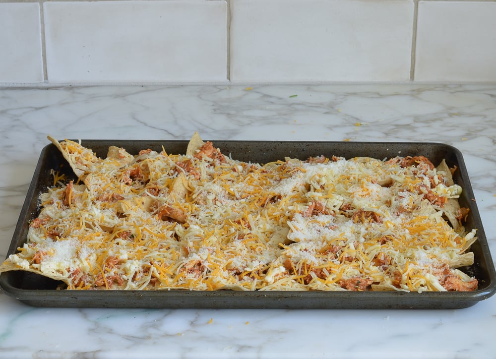Shredded cheese on a baking sheet of tortilla chips and chicken.