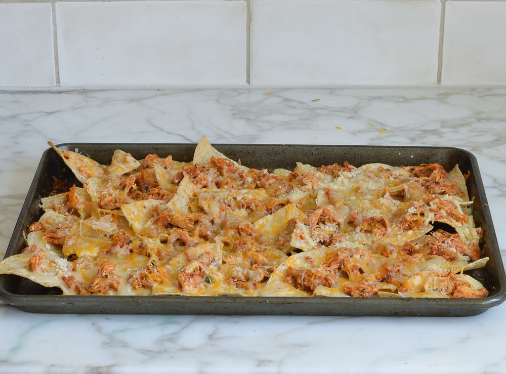 Sheet pan of chicken nachos with melted cheese.