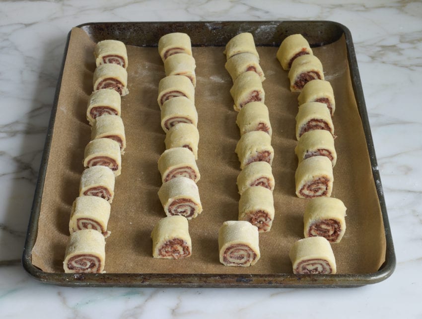 Uncooked chocolate rugelach on a lined baking sheet.