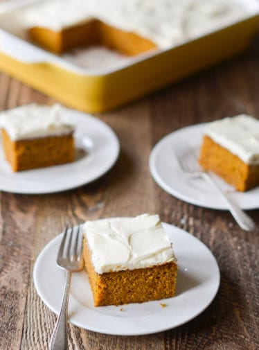 Slices of pumpkin cake with cream cheese frosting on small plates with forks.