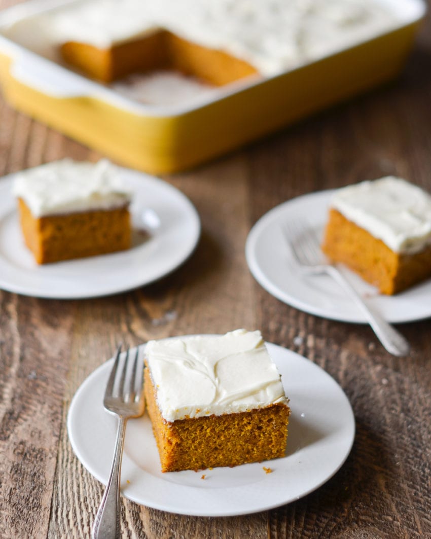 Slices of pumpkin cake with cream cheese frosting on small plates with forks.