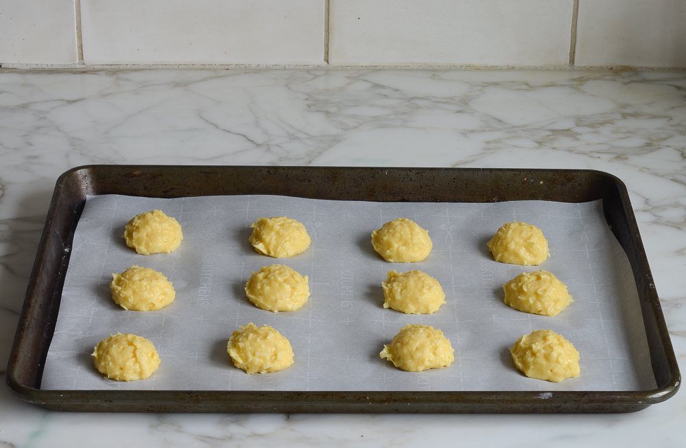 Mounds of gougeres dough on a lined baking sheet.