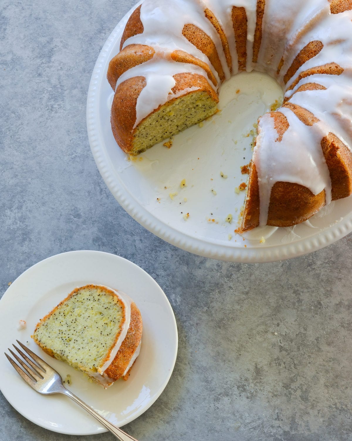 Glazed lemon poppy seed cake on a platter with slices missing.