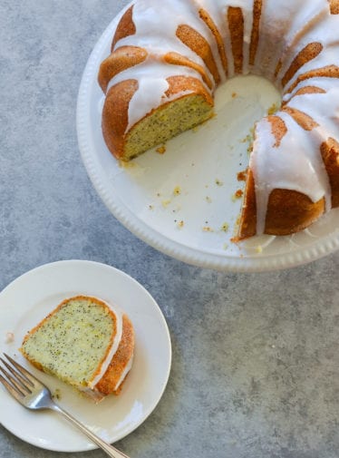 Slice of lemon poppy seed cake next to the rest of the cake.