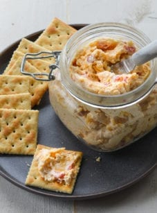 Jar of pimento cheese on a plate with crackers.