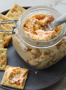 Jar of pimento cheese on a plate with crackers.