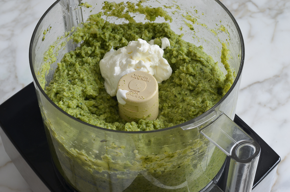 Sour cream in a food processor with processed broccoli.