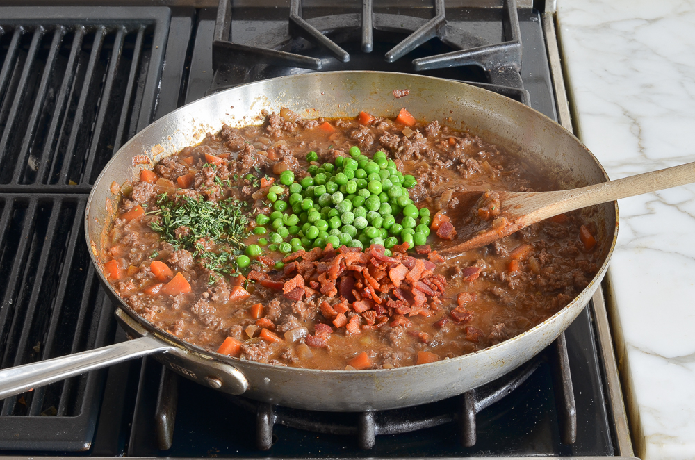 adding the peas, thyme and bacon to the stew