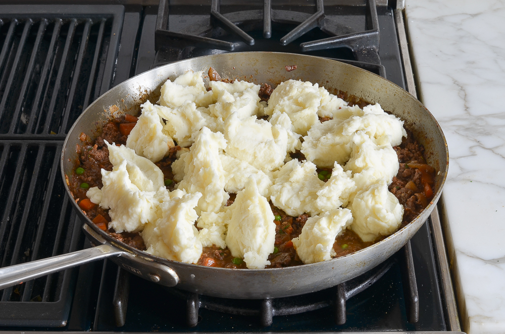 dolloping the mashed potatoes over the stew in the skillet