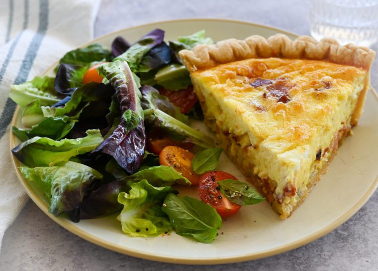 Slice of quiche lorraine on a plate with a salad.