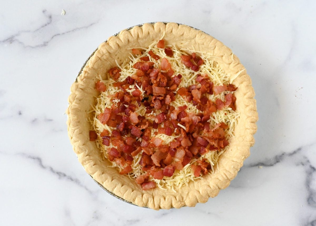 Diced bacon on shredded gruyere in a pie crust.