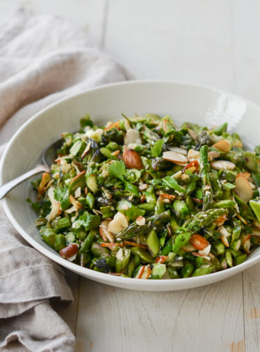 Spoon in a bowl of raw asparagus salad with almonds and ginger-sesame vinaigrette.