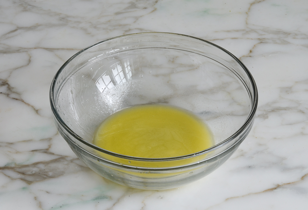 melted butter and chocolate mixed together with wooden spoon in medium glass bowl