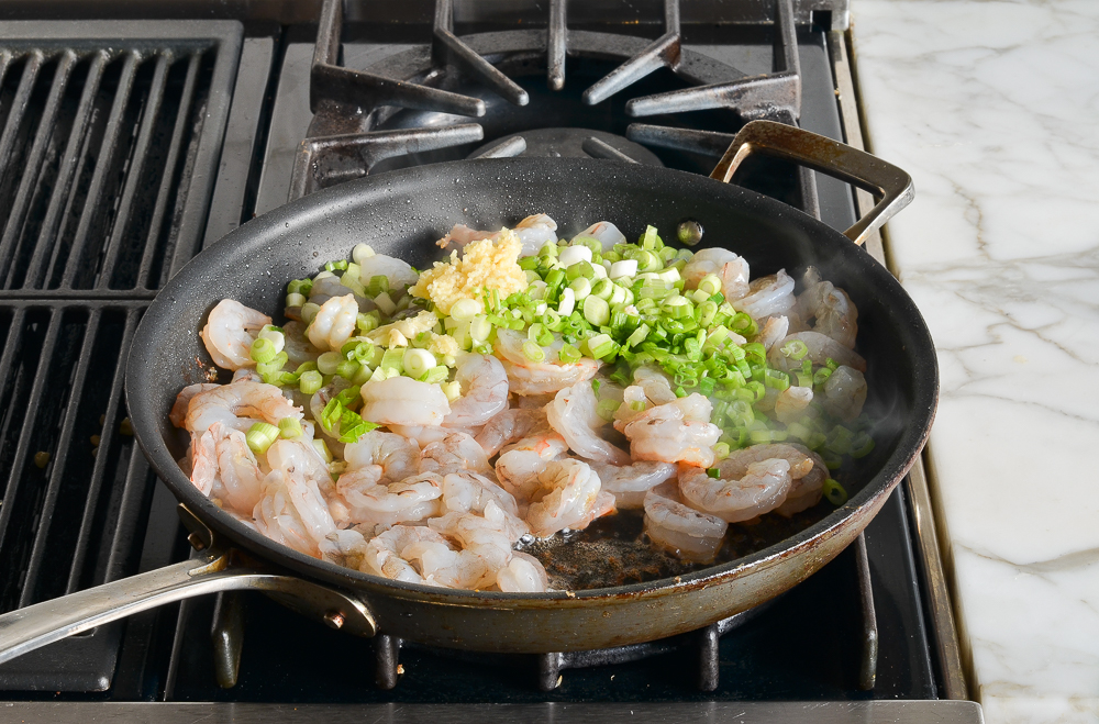 adding the shrimp, scallions, garlic, cumin, chili powder and salt to pan