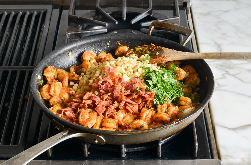 adding the corn, bacon, lime, and cilantro to the shrimp