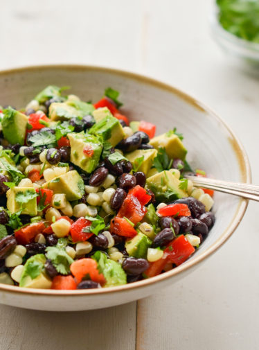 Spoon in a bowl of black bean salad with corn, avocado, and lime vinaigrette.