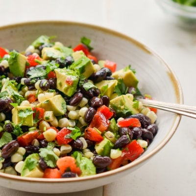 Spoon in a bowl of black bean salad with corn, avocado, and lime vinaigrette.