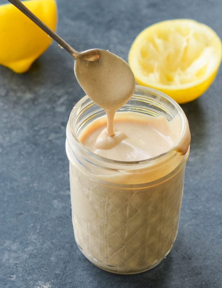 Spoon dripping tahini sauce into a glass jar.