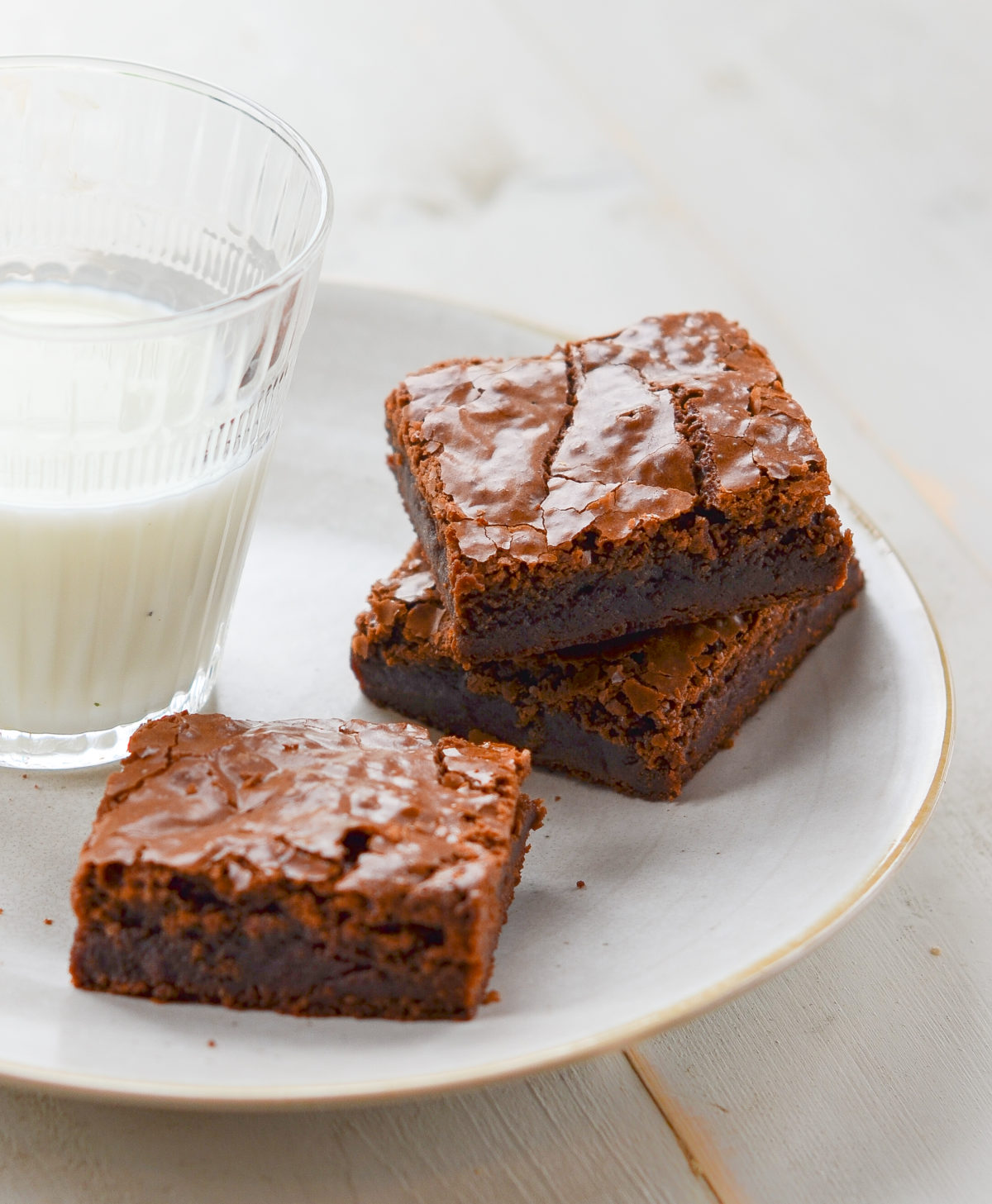 Three brownies on a plate with a glass of milk.