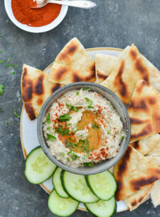 Bowl of baba ganoush on a plate with cucumbers and bread.