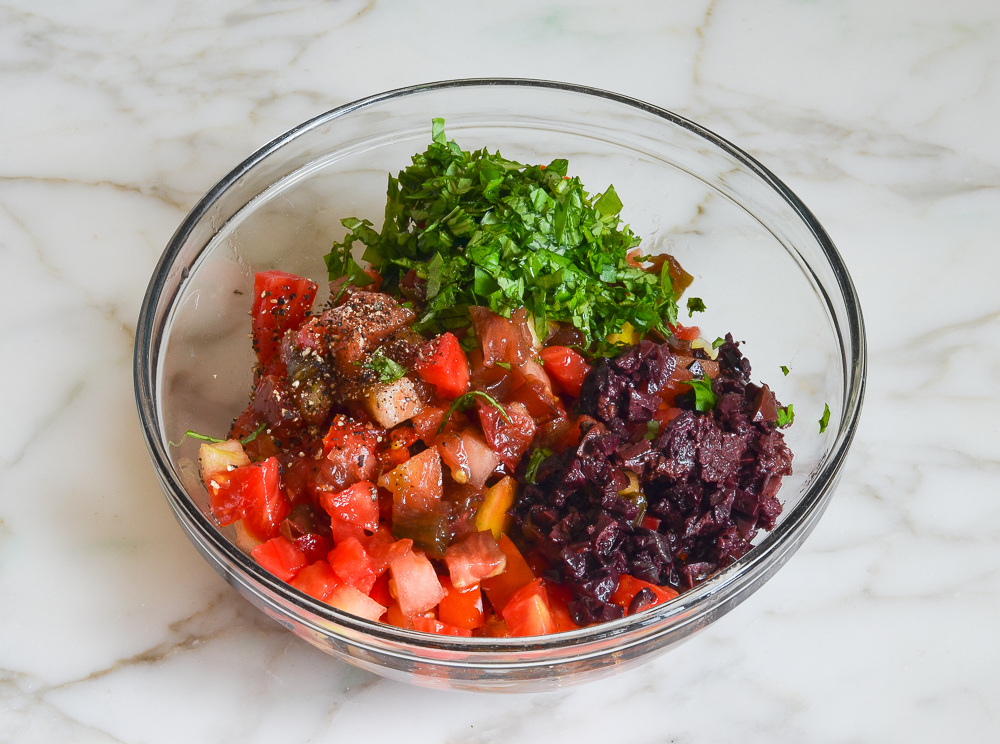 combining tomatoes, olives, basil, and seasonings in bowl