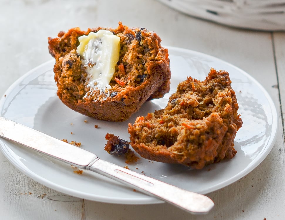 Halved morning glory muffin smeared with butter on plate.